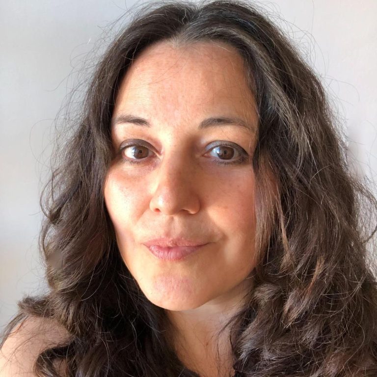 Mujer de cabello rizado, mirando a la cámara con expresión amigable.