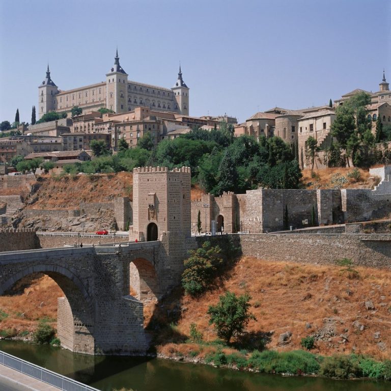Puente sobre el río con vistas al Alcázar y edificios históricos en Toledo.