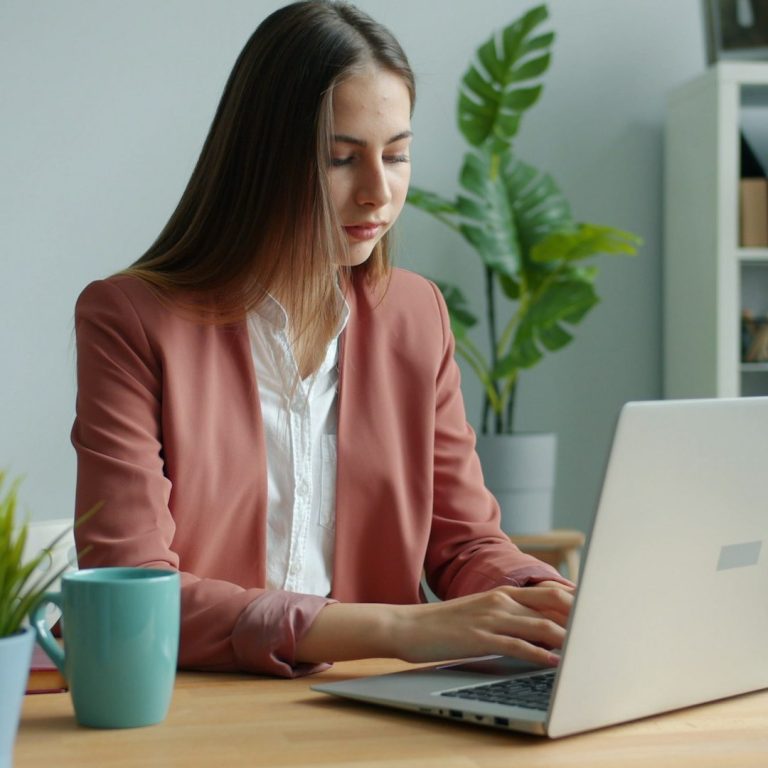 Mujer en un entorno de oficina, trabajando en una laptop con una taza de café.