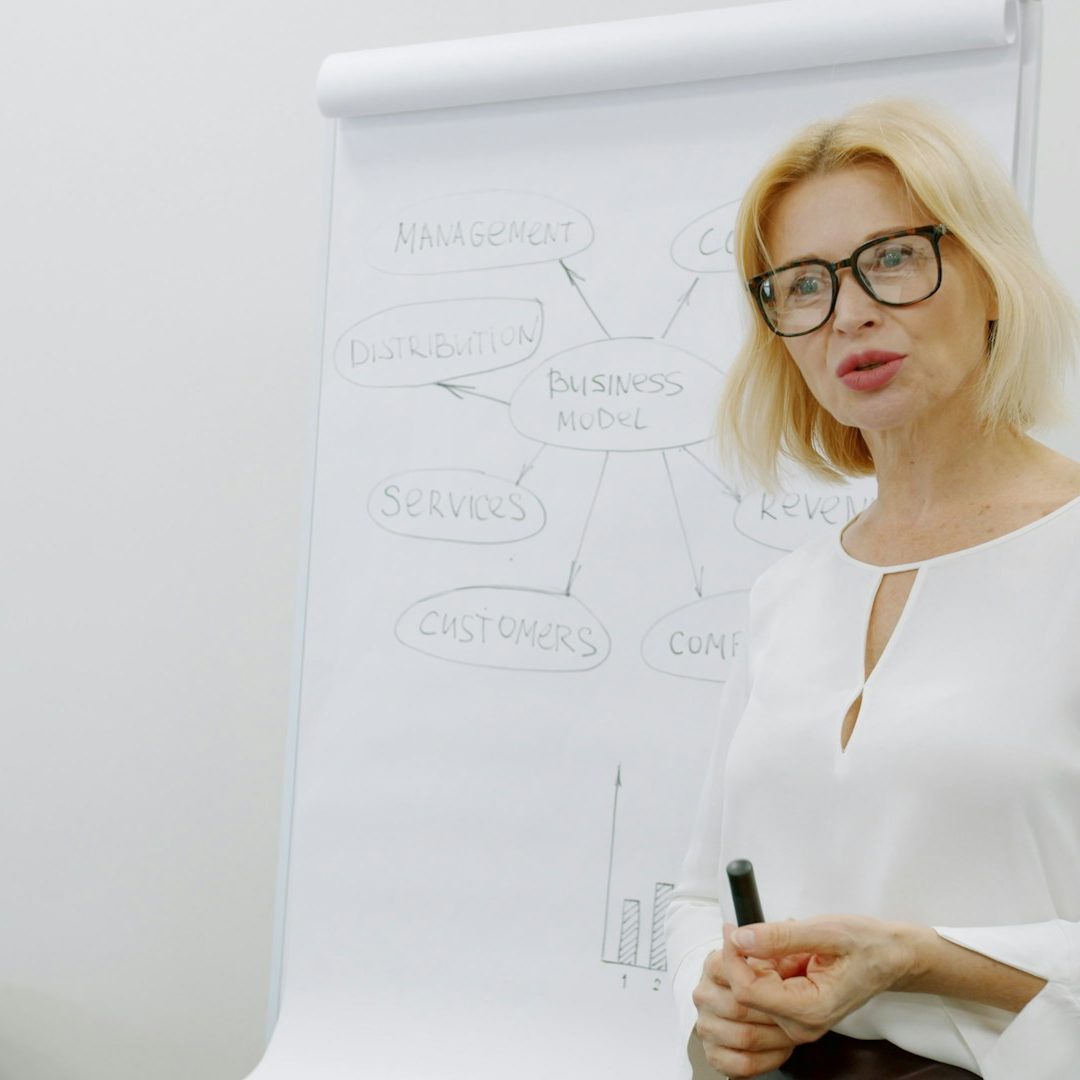 Mujer rubia con gafas presentando información ante un panel de gráficos en un entorno profesional.