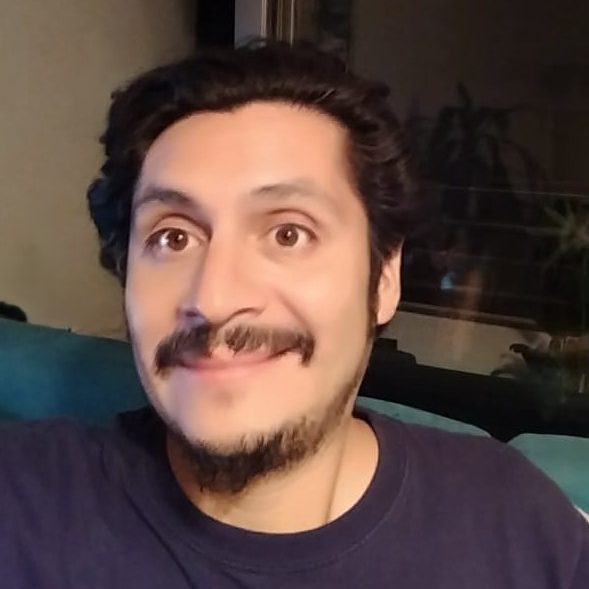 Hombre sonriente con cabello rizado, usando una camiseta oscura, posando en un entorno interior.