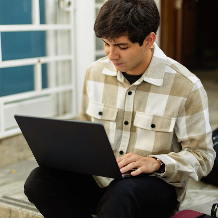 Hombre joven sentado en escaleras, trabajando en un portátil.
