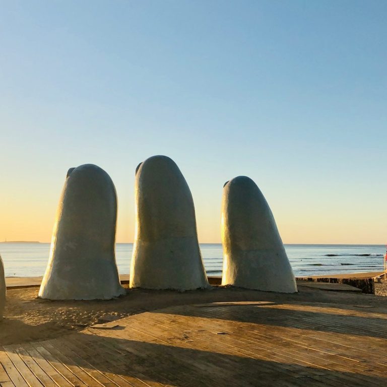 Esculturas en forma de manos en la playa durante el atardecer. Mar al fondo.